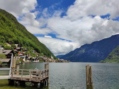 A magical landscape in Austria featuring a serene lake surrounded by majestic mountains, under a sky filled with fluffy clouds that reflect the beauty of nature. clipart