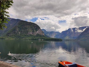 A magical landscape in Austria featuring a serene lake surrounded by majestic mountains, under a sky filled with fluffy clouds that reflect the beauty of nature. clipart