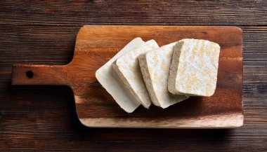 Ahşap kesim tahtasındaki çiğ tempeh ya da tempo, ahşap bir arka planda izole edilmiş.