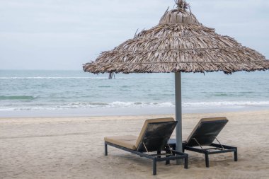 Pair of deck chairs under a palm umbrella in beautiful Cua Dai Beach in Hoi An, Central Vietnam