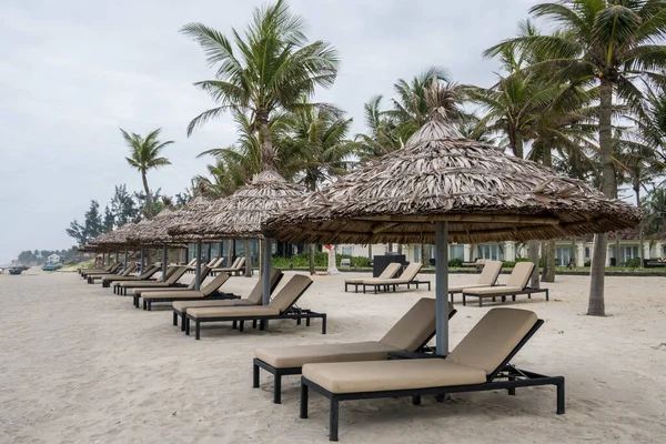 Row of deck chairs under a palm umbrella in beautiful Cua Dai Beach in Hoi An, Central Vietnam