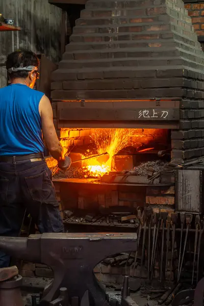 Chishang, Tayvan - 9 Aralık 2023: Demirci ve metal ocağı bir kılıcı ısıtmak için bir patlama fırını kullanıyor..