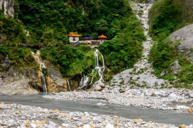 Eternal Spring Shrine or Changchun Shrine in Taroko National Park in Taiwan: The temple is nestled on a lush green mountainside with picturesque waterfalls flowing into a rocky river clipart