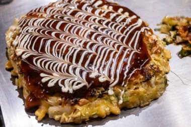 Japon lezzetli krepi Okonomiyaki 'nin yakın çekimi. Üstünde okonomi sosu ve mayonez var. Krepte lahana ve diğer malzemeler var..