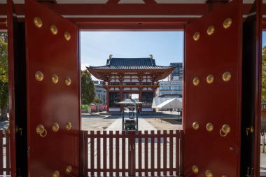 Open red temple gates reveal a traditional Japanese pagoda gate Grand West Gate and courtyard at Shitenno-ji Temple in Osaka, Japan clipart