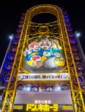Osaka, Japonya - 16 Mart 2024: Dotonbori, Osaka 'da gece aydınlatılmış dönme dolap. Çizgi film karakterli, gülümseyen bir adamın büyük bir heykeli.. 