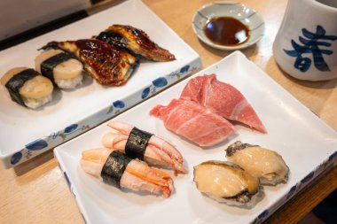 Beyaz tabakta çeşitli suşi nigiri unagi balığı, ton balığı, istiridye ve yengeç. Soya sosu ve seramik bardak yakınlarda.. 