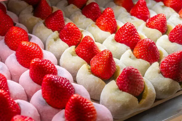 Daifuku sıraları - çilekli mochi, yumuşak, soluk pirinç keklerinin içine yerleştirilmiş canlı kırmızı çilekler sergileniyor. İki mochi varyasyonu görünür.