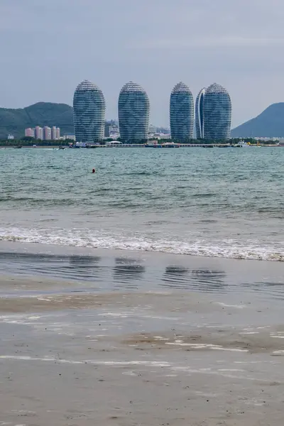 Sanya, Hainan, Çin 'deki Phoenix Adası' nda beş uzun ve ince binayla kıyı şehrine bakan panoramik bir manzara. Suda tekneler ve gemiler var.