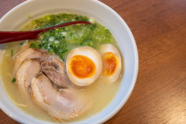 Bir kase tonkotsu ramen, içinde taze domuz dilimleri, yarı haşlanmış yumurta, yumurta sarısı, yeşil soğan ve hafif et suyu. Beyaz bir kasede servis edilmiş..