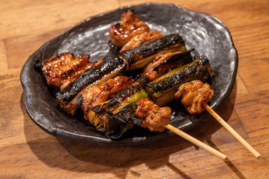 Izgara yakitori tabağı. İçinde tavuk parçaları ve kömürleşmiş soğanlar var. Bol, koyu bir sos ile kaplanmış..