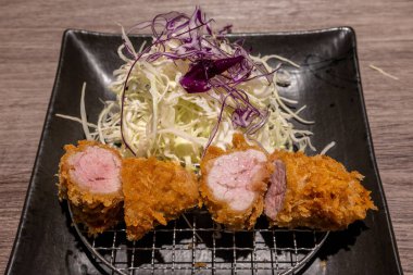Japon Tonkatsu - Dilimlenmiş domuz filetosu, altın kahverengi ve çıtır çıtır, öğütülmüş lahana ve mor lahana ile birlikte siyah bir tabakta servis edilir.. 