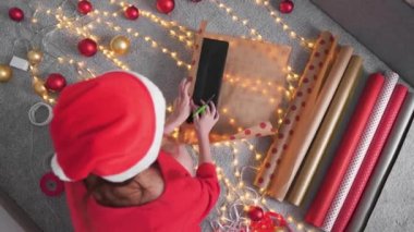 Genç bir kadın arkadaşları ve akrabaları için Noel hediyesi paketliyor. Kız kırmızı kağıtlı, renkli kurdeleli yeni yıl paketleri yapıyor. Noel süslemeleri, tatil sezonu hazırlıkları..