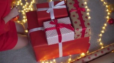 Genç bir kadın arkadaşları ve akrabaları için Noel hediyesi paketliyor. Kız kırmızı kağıtlı, renkli kurdeleli yeni yıl paketleri yapıyor. Noel süslemeleri, tatil sezonu hazırlıkları..