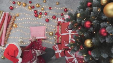 Noel ağacı ve şöminenin yanındaki Noel ışıklarının arka planında bir sürü güzel Noel hediyesi kutusunun yanında genç bir kadın. Atmosfer ve yeni yıl havası, altın ve kırmızı renkli şenlik dekoru..