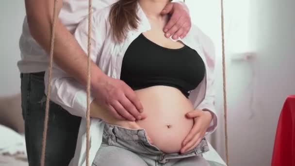 快乐的孕妇 大肚子在家里休息 怀孕的年轻女人和一个怀上孩子的男人年轻的孕妇爱抚她的肚子 这个年轻的家庭正在等待补给 — 图库视频影像