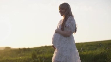 Beyaz gömlekli, elbiseli, öpüşen, sarılan, doğada, ağacın yanında göbeğine dokunan genç, mutlu, romantik bir çift. Hamile kadın bir bebek bekliyor. Müstakbel anne ve baba, aile.