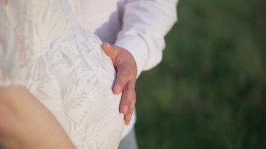 Beyaz gömlekli, elbiseli, öpüşen, sarılan, doğada, ağacın yanında göbeğine dokunan genç, mutlu, romantik bir çift. Hamile kadın bir bebek bekliyor. Müstakbel anne ve baba, aile.