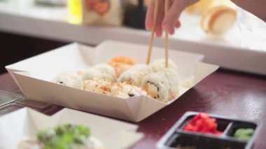 İnsanlar evde mutfakta suşi yiyorlar. Japon yemekleri eşliğinde arkadaşlarla ortak toplantılar. Aile yemeği ve suşi teslimatı. Somon, yengeç, wasabi, zencefil, peynir.