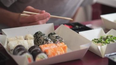 İnsanlar evde mutfakta suşi yiyorlar. Japon yemekleri eşliğinde arkadaşlarla ortak toplantılar. Aile yemeği ve suşi teslimatı. Somon, yengeç, wasabi, zencefil, peynir.