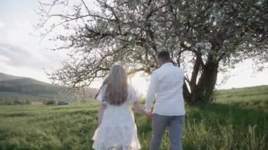 Mutlu çift sahada günbatımının arka planında eğleniyor. Birbirine aşık bir erkek ve kız yazın doğada yürüyor, sarılıyor ve dinleniyorlar. El ele tutuşup, gün batımını seyrediyorum..