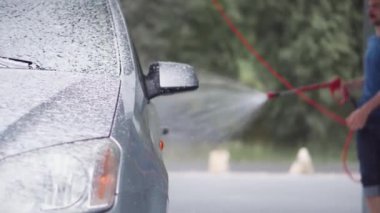 Bir adam oto yıkamada araba yıkar. Genç bir adam arabayı basınç altında köpük ve suyla temizler ve bir bezle siler. Gri bir arabayı özen ve yaz elle yıkama.