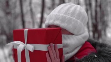Karda kırmızı hediye kutusu olan bir kadın. Kışın yeni yıl tatilinde Aralık ayında bir kız. Soğuk kışta insanlar dışarıda. Noel alışverişi ve kışın kırmızı pelerinli karlı ormanda yürüyüş..