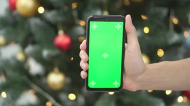 Kroma tuşuna yeşil ekran takılı akıllı telefon. Noel arkaplanındaki yeni yıl şenlikli yılbaşı ağacı arka planda bulanık ışıklar. Terfi, online alışveriş, iş.