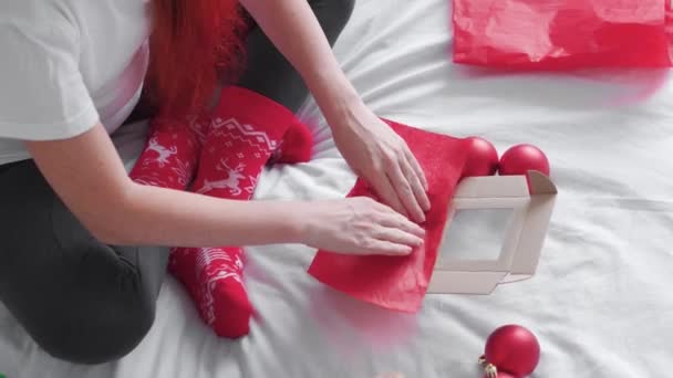女人们手拿着礼品盒 为节日准备一个惊喜 这个女孩在床上做了一件漂亮的新年礼物 最好的圣诞礼物红色玩具球 包装纸和圣诞帽 — 图库视频影像