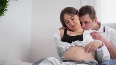 Kocası bebek bekleyen hamile, genç bir kadın. Genç aile tazeleme için bekliyor. Koca göbekli mutlu hamile kadın evde dinleniyor. Genç hamile anne karnını okşar..