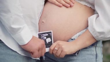 Güzel hamile bir kadın ve kocası karnındaki bir bebeğin fotoğrafına bakıyorlar. Müstakbel anne ve babaları ilk çocuklarının doğmasını bekliyorlar. Hamilelik ve mutluluk