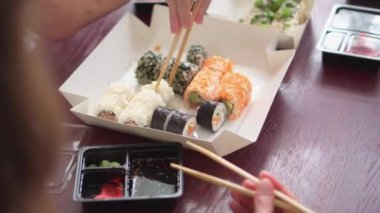Japon yemekleri eşliğinde arkadaşlarla ortak toplantılar. İnsanlar evde mutfakta suşi yiyorlar. Aile yemeği ve suşi teslimatı. Somon, yengeç, wasabi, zencefil, peynir.