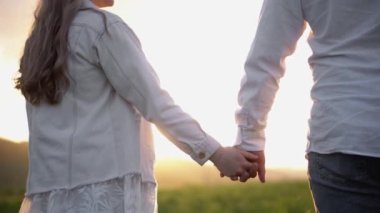 Birbirine aşık bir erkek ve kız yazın doğada yürüyor, sarılıyor ve dinleniyorlar. Sahada günbatımının arka planında eğlenen mutlu çift. El ele tutuşup, güneşin doğuşunu seyrediyorum..