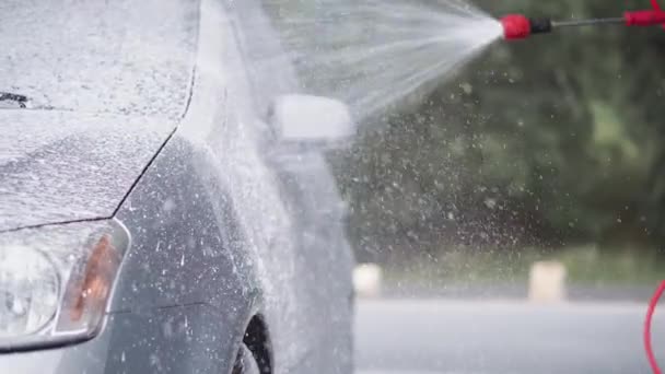 一个年轻人用泡沫和加压的水清洗汽车 并用抹布擦拭 一名男子在自助洗车时洗车 小心和夏季手工洗车 颜色为灰色 — 图库视频影像
