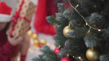Arka planda Noel ışıkları, çelenkler ve şöminenin üzerinde Noel hediyesi kutuları olan bir kız. Genç bir kadın yeni yıl arifesinde hediyeleri ağacın yanında renkli kırmızı kağıtlarla sarar. Atmosfer havası, dekor kışı.