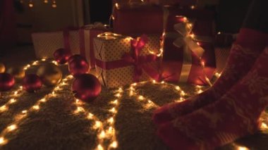 Arka planda Noel ışıkları, çelenkler ve şöminenin üzerinde Noel hediyesi kutuları olan bir kız. Genç bir kadın yeni yıl arifesinde hediyeleri ağacın yanında renkli kırmızı kağıtlarla sarar. Atmosfer havası, dekor kışı.