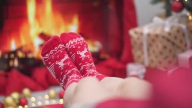 Arka planda Noel ışıkları, çelenkler ve şöminenin üzerinde Noel hediyesi kutuları olan bir kız. Genç bir kadın yeni yıl arifesinde hediyeleri ağacın yanında renkli kırmızı kağıtlarla sarar. Atmosfer havası, dekor kışı.