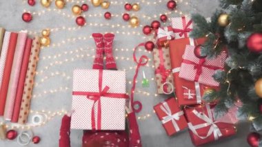 Arka planda Noel ışıkları, çelenkler ve şöminenin üzerinde Noel hediyesi kutuları olan bir kız. Genç bir kadın yeni yıl arifesinde hediyeleri ağacın yanında renkli kırmızı kağıtlarla sarar. Atmosfer havası, dekor kışı.