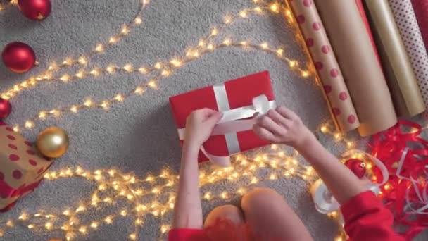 Dziewczyna Kapeluszu Mikołaja Tworzy Pakiety Sylwestrowe Czerwonego Papieru Pakowania Młoda — Wideo stockowe