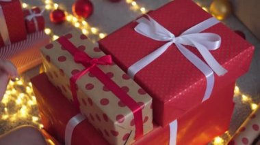 Noel Baba şapkalı bir kız kırmızı ambalaj kağıdından yeni yıl paketleri yapıyor. Genç kadın arkadaşları ve akrabaları için Noel hediyesi paketliyor. Dekorasyon, kış tatili için hazırlık.