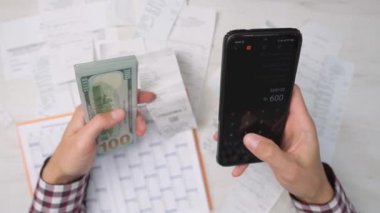 Bir kişi akıllı telefon hesap makinesi kullanarak faturaları ve faturaları hesaplar. Bir adam nakit olarak para sayar, avro olarak. Mal ve hizmetler ve maaş harcamalarının özeti ve analizi.