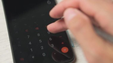 Bir kişi akıllı telefon hesap makinesi kullanarak faturaları ve faturaları hesaplar. Bir adam nakit olarak para sayar, avro olarak. Mal ve hizmetler ve maaş harcamalarının özeti ve analizi.