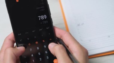 Bir kişi akıllı telefon hesap makinesi kullanarak faturaları ve faturaları hesaplar. Bir adam nakit olarak para sayar, avro olarak. Mal ve hizmetler ve maaş harcamalarının özeti ve analizi.