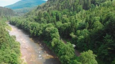 Yazın Ukrayna Karpatları gezisi. Büyük bir turist arabası. Dağlar, nehirler ve yeşil ormanlar arasında doğada çekilen hava görüntüleri. Kamyon bir dağ yolunda turist yolunda ilerliyor.