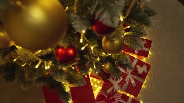 ライト ボールやプレゼントで飾られたクリスマスツリー 新年の休日の雰囲気 冬のおとぎ話や自宅でクリスマスの精神 緑の木の下にリボン付きの赤いパッケージをプレゼント スローモーション — ストック動画