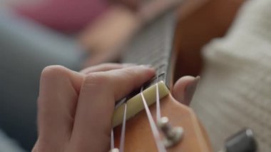 Ukulele kadınların elinde. Bir kadın evde kanepede otururken ukulele çalmayı öğrenir. Kız küçük bir gitarda ukulele çalıyor ve şarkı söylüyor. Hobi ve müzik aleti konsepti.