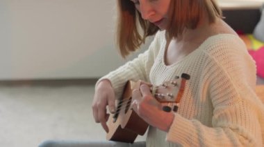 Ukulele kadınların elinde. Bir kadın evde kanepede otururken ukulele çalmayı öğrenir. Kız küçük bir gitarda ukulele çalıyor ve şarkı söylüyor. Hobi ve müzik aleti konsepti.