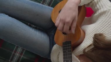 Ukulele kadınların elinde. Bir kadın evde kanepede otururken ukulele çalmayı öğrenir. Kız küçük bir gitarda ukulele çalıyor ve şarkı söylüyor. Hobi ve müzik aleti konsepti.