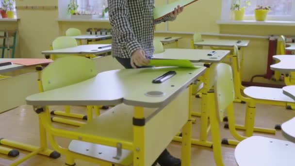 一位女教师在教室里走来走去 把几张纸铺在桌子上 这个女孩是个在校学生 孩子的教育的内部 孩子的教育观念 — 图库视频影像