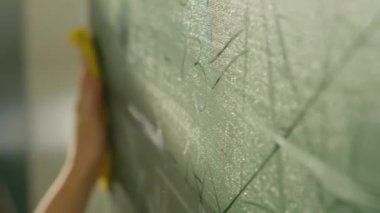 A girl student writes on a green board. Female teacher near the school board. A hand writes information on the board with white chalk. Concept of educational process, demonstration.